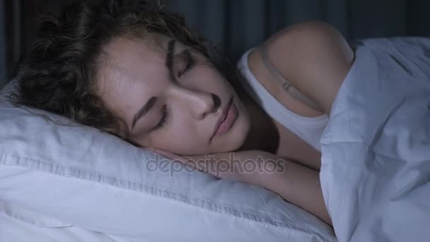 Красива молода жінка спить у темній спальні вночі — стокове відео