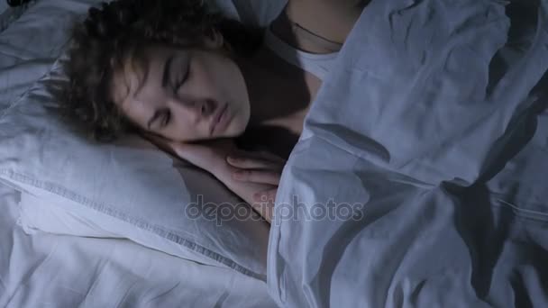 Спящая женщина просыпается и покидает кровать в темной комнате ночью — стоковое видео