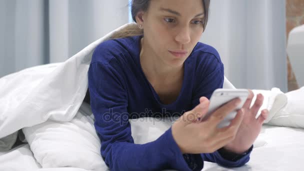 オンラインを閲覧するための携帯電話を使用してベッドに横たわっているヒスパニック系の女性 — ストック動画