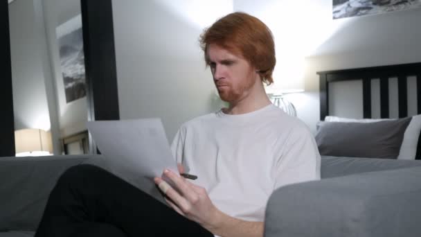 Penisve vörös hajú ember olvasás levelet, ül a kanapén — Stock videók