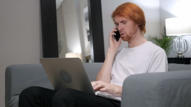 Ruiva homem falando no telefone enquanto trabalhando no laptop — Vídeo de Stock