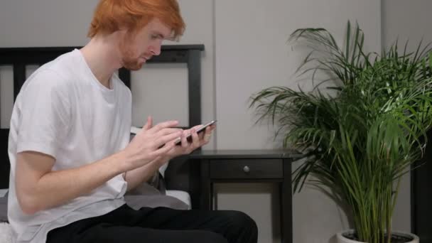 Smartphone nutzen und auf Erfolg reagieren, im Bett sitzen — Stockvideo