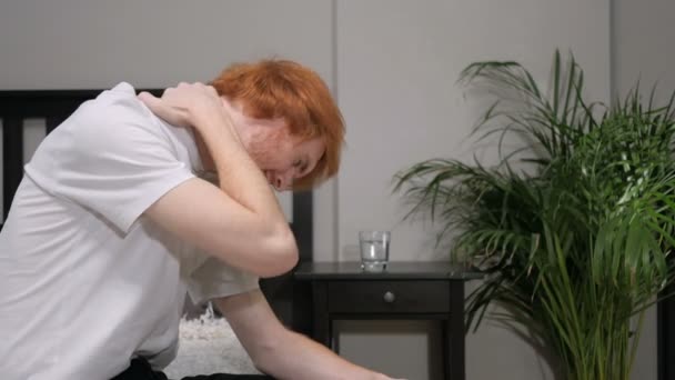 Yatak, ağrı boyun tarafında oturan yorgun Kızıl saçlı adam — Stok video