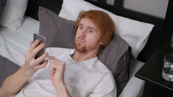 Roodharige Man liggend in Bed met behulp van Internet op Smartphone — Stockvideo