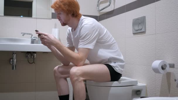 Рыжий с помощью смартфона в туалете, Commode — стоковое видео