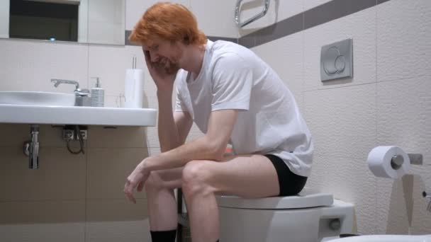 Напряженный рыжеволосый мужчина сидит в туалете, Commode — стоковое видео