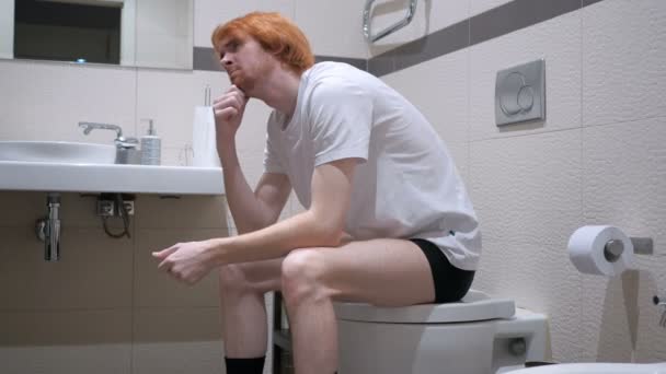 Denkender Rotschopf sitzt in Badezimmerkommode — Stockvideo