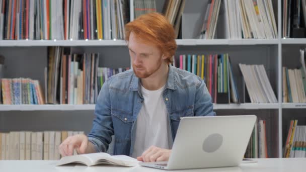 Roodharige Man lezen boek, zittend in de bibliotheek — Stockvideo