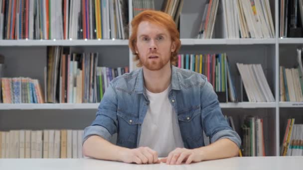 Человек с рыжими волосами указывает на камеру в библиотеке — стоковое видео