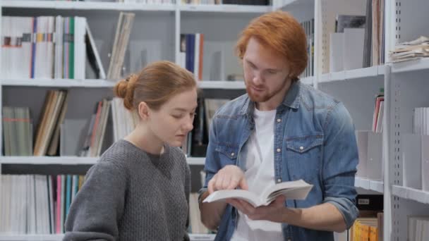 Estudiantes sonrientes positivos leyendo libro y discutiendo en la biblioteca — Vídeo de stock