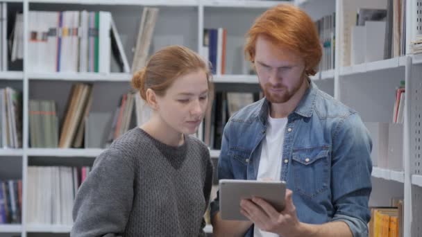 Молодые товарищи по команде, студенты просматривают планшетный компьютер в библиотеке, работа — стоковое видео