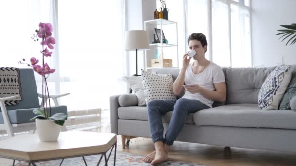 Ο άνθρωπος πίνοντας καφέ ενώ κάθεται στον καναπέ στο σπίτι — Αρχείο Βίντεο