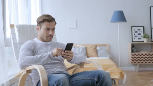 Homem adulto ocupado usando Smartphone enquanto relaxa na cadeira — Vídeo de Stock