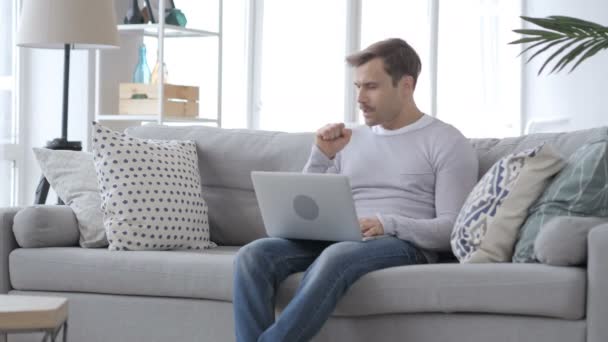 Tos, Hombre tosiendo mientras trabaja en el ordenador portátil en el sofá — Vídeo de stock