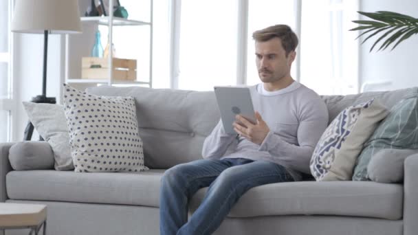 Серйозна людина використовує планшет сидячи на дивані — стокове відео