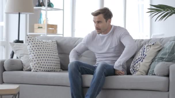 Дорослий чоловік сидить на дивані виходячи з кімнати — стокове відео