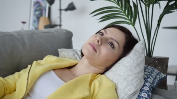 Расслабляющая молодая женщина лежит на диване дома — стоковое видео