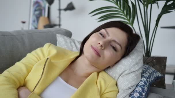 Lächelnde junge Frau blickt in die Kamera, während sie zu Hause auf dem Sofa liegt — Stockvideo