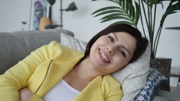 微笑的女人看着相机, 而躺在沙发上在家 — 图库视频影像