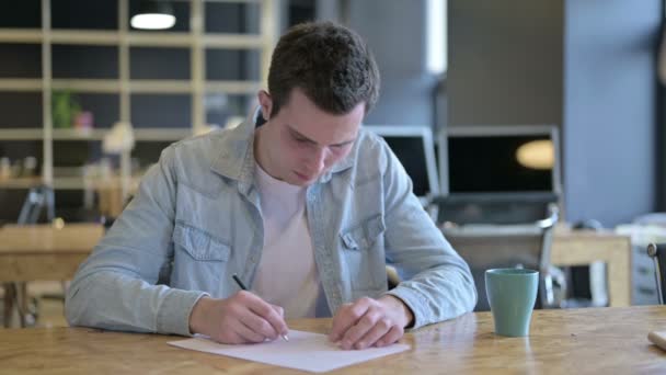 Jonge ontwerper denken en schrijven op papier in het moderne kantoor — Stockvideo