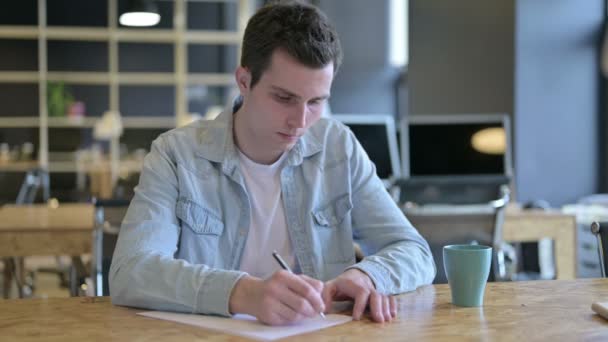 Трудолюбивый молодой дизайнер читает документы в современном офисе — стоковое видео