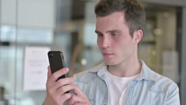 Retrato de triste joven diseñador recibiendo la pérdida en el teléfono inteligente — Vídeo de stock