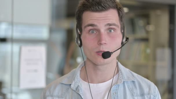 Retrato de un joven empleado del centro de llamadas hablando con auriculares — Vídeo de stock