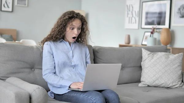 Šokovaná Kadeřnatá žena práce na laptopu, Sezení na gauči — Stock fotografie