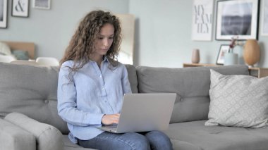 Kanepede otururken kıvırcık saç kadın laptop üzerinde çalışma