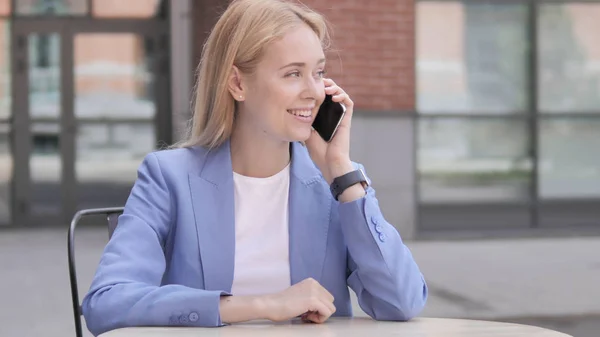 Молодая предпринимательница разговаривает по телефону сидя на открытом воздухе — стоковое фото