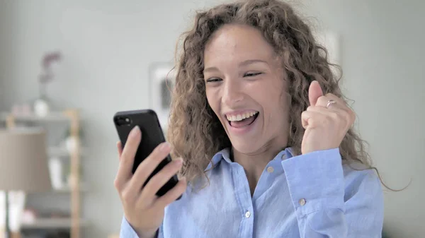 Emocionado cabello rizado mujer disfrutando del éxito mientras se utiliza el teléfono inteligente — Foto de Stock