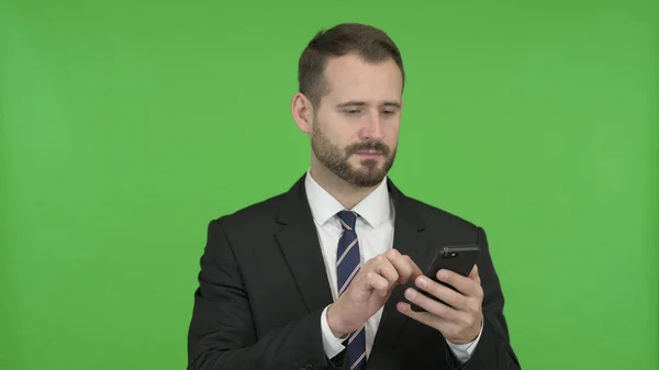 De vrolijke zakenman scrollt zijn mobiele telefoon tegen Chroma Key — Stockfoto