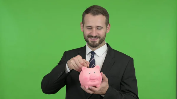 Wesoły biznesmen oddanie pieniędzy w Piggy Bank przeciw Chroma Key — Zdjęcie stockowe
