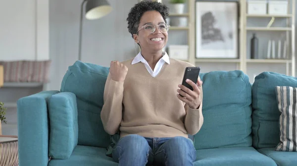 Веселая девушка, сидящая на диване, пользуется телефоном — стоковое фото
