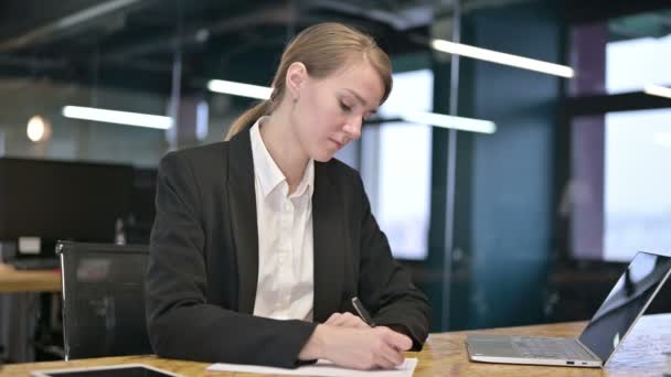 Joven empresaria enfocada a escribir sobre papel en la oficina moderna — Vídeo de stock