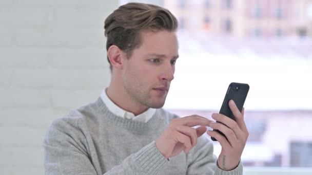 Retrato de triste joven creativo reaccionando a la pérdida en el teléfono inteligente — Vídeo de stock