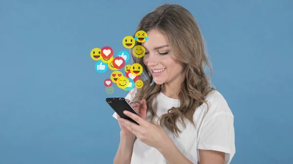 Mavi Arkaplanda Akıllı Telefon Kullanan Genç Kadın, Uçan Gülücükler, Emojiler ve Sevenler