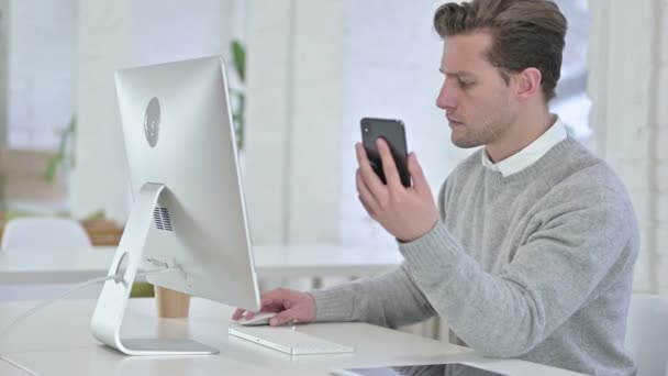 Joven trabajando en el escritorio y usando Smartphone — Vídeos de Stock