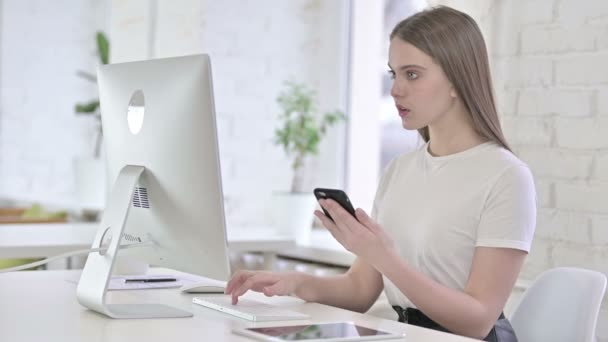 Привлекательная молодая женщина, использующая смартфон и работающая на рабочем столе — стоковое видео