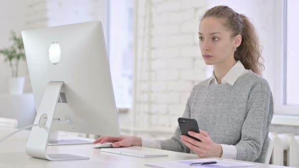 Jovem mulher latina atraente usando Smartphone e trabalhando no iMac — Vídeo de Stock