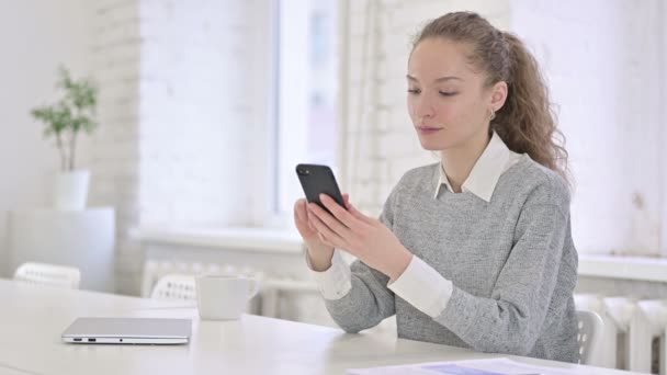 Ontspannen Jonge Latijnse vrouw met behulp van Smartphone in Modern Office — Stockvideo