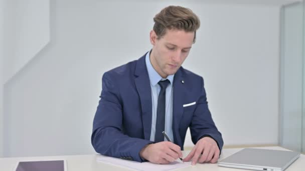 Серьезный молодой бизнесмен занимается бумажной работой в офисе — стоковое видео