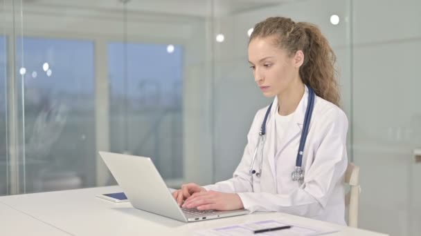 Fröhliche junge Ärztin arbeitet im Büro am Laptop — Stockvideo