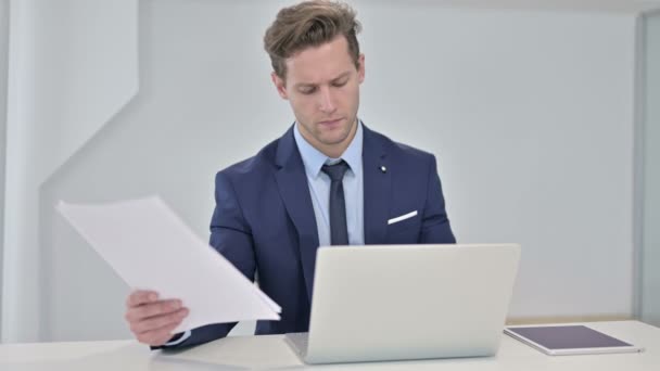 Joven Empresario Leyendo Documentos y Trabajando en Laptop — Vídeos de Stock