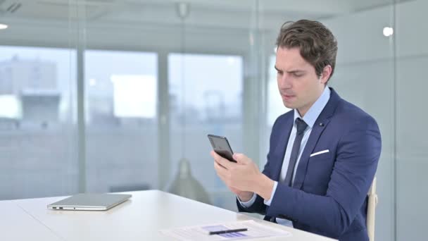 Profesionální mladý podnikatel používající chytrý telefon v moderní kanceláři — Stock video