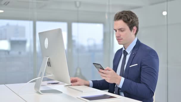 Joven Empresario Hablando en Smartphone y Trabajando en Desk Top — Vídeo de stock