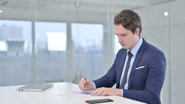 Ernstige jonge zakenman doet papierwerk in Office — Stockvideo