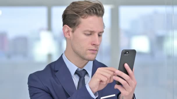 Portrét veselého mladého podnikatele pomocí chytrého telefonu v kanceláři — Stock video