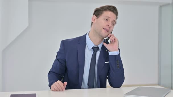 Attraktiver junger Geschäftsmann, der im Büro mit dem Smartphone spricht — Stockvideo