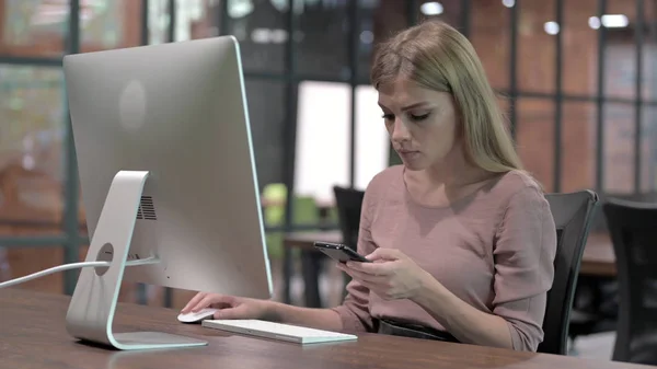 Fiatal nő használ Smartphone miközben ül Office Desk — Stock Fotó